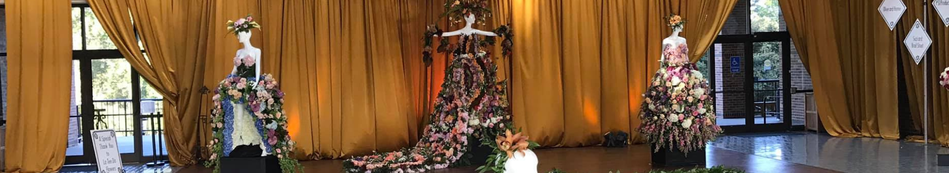 Three mannequins with dresses made of roses in front of gold curtains at the Tyler Rose Garden Center